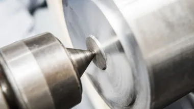 Zbliżenie na metalowy element obrabiany przez stożkowe narzędzie tokarki.