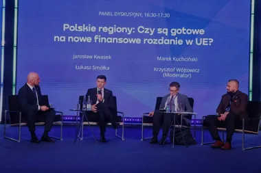 Czterech mężczyzn uczestniczy w panelu dyskusyjnym na scenie z niebieskim tłem z tematyką finansową UE.