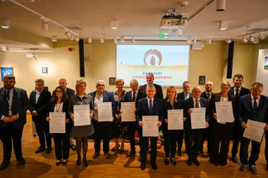 Grupa osób w sali konferencyjnej trzyma dokumenty z napisem „AKT POWOŁANIA” podczas uroczystości związanej z „Karpackim Pierścieniem Naukowym”.