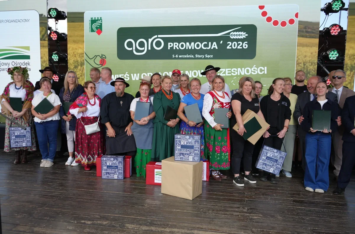 Grupa osób pozuje do pamiątkowego zdjęcia na scenie podczas wydarzenia Agro Promocja 2026 w Starym Sączu, trzymając dyplomy i nagrody.